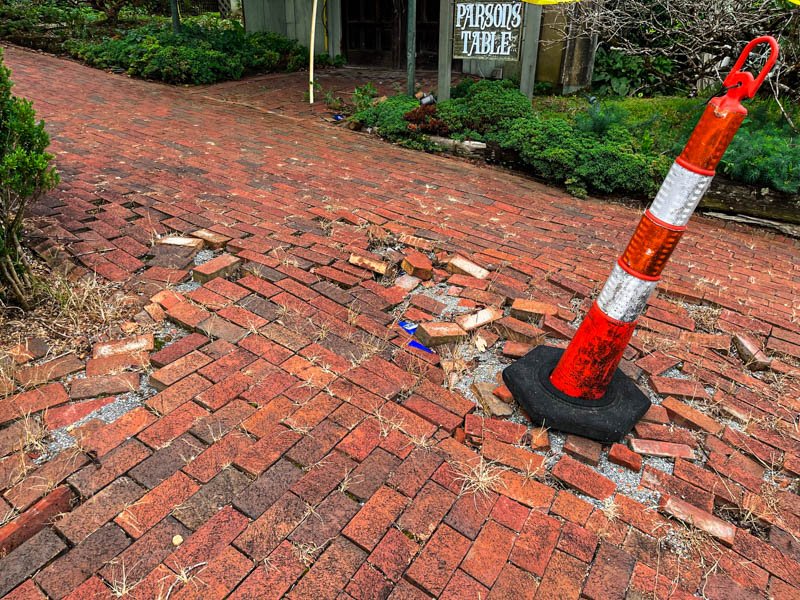 broken bricks and a safety pylon mark a dangerous sidewalk